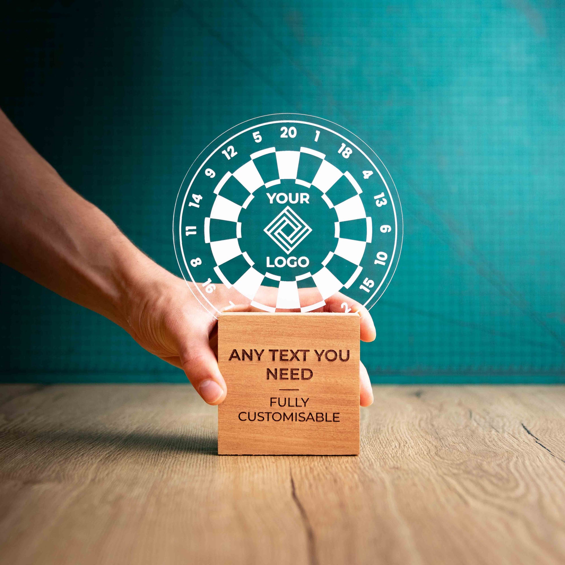 A hand holding a large darts trophy with custom text and logos, on an eco-friendly wooden base, with a clear Perspex dart board mounted on top, featuring fully customisable areas for text and logos.