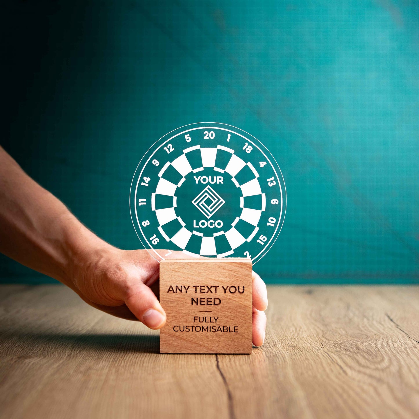 A hand holding a large darts trophy with custom text and logos, on an eco-friendly wooden base, with a clear Perspex dart board mounted on top, featuring fully customisable areas for text and logos.