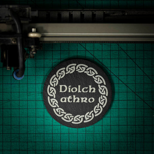 A Welsh slate coaster laser engraved with the welsh word for thank you teacher diolch athro, inside a celtic knot