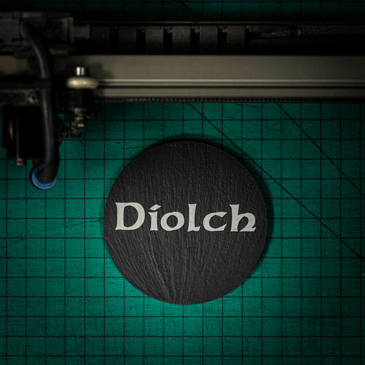 A Welsh slate coaster laser engraved with the welsh word for thank you, diolch