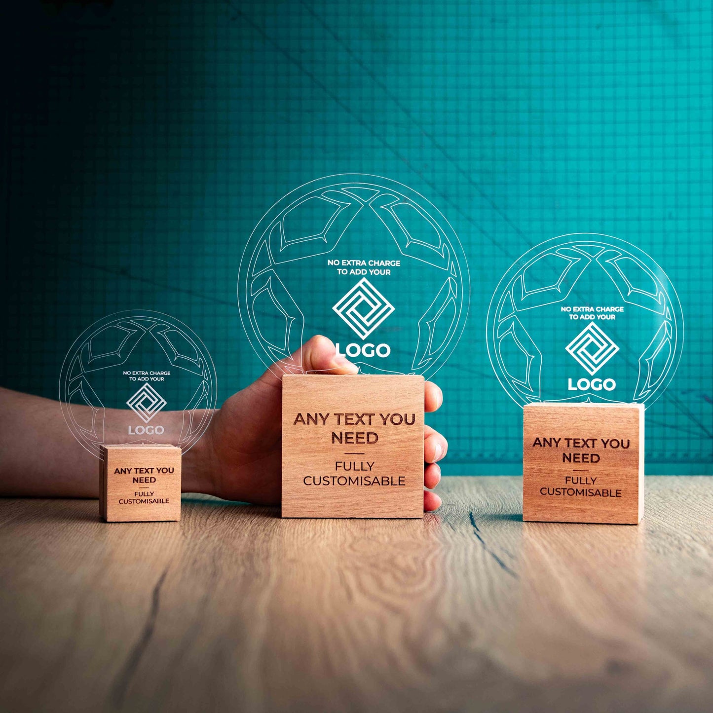 A hand holding a large football trophy, with small and medium versions on either side, custom text and logos, eco-friendly wooden bases, and a clear Perspex football mounted on top, with fully customisable areas featuring text and logos.