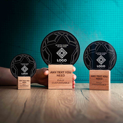 A hand holding a large football trophy, with small and medium versions on either side, custom text and logos, eco-friendly wooden bases, and a clear Perspex football mounted on top, with fully customisable areas featuring text and logos.