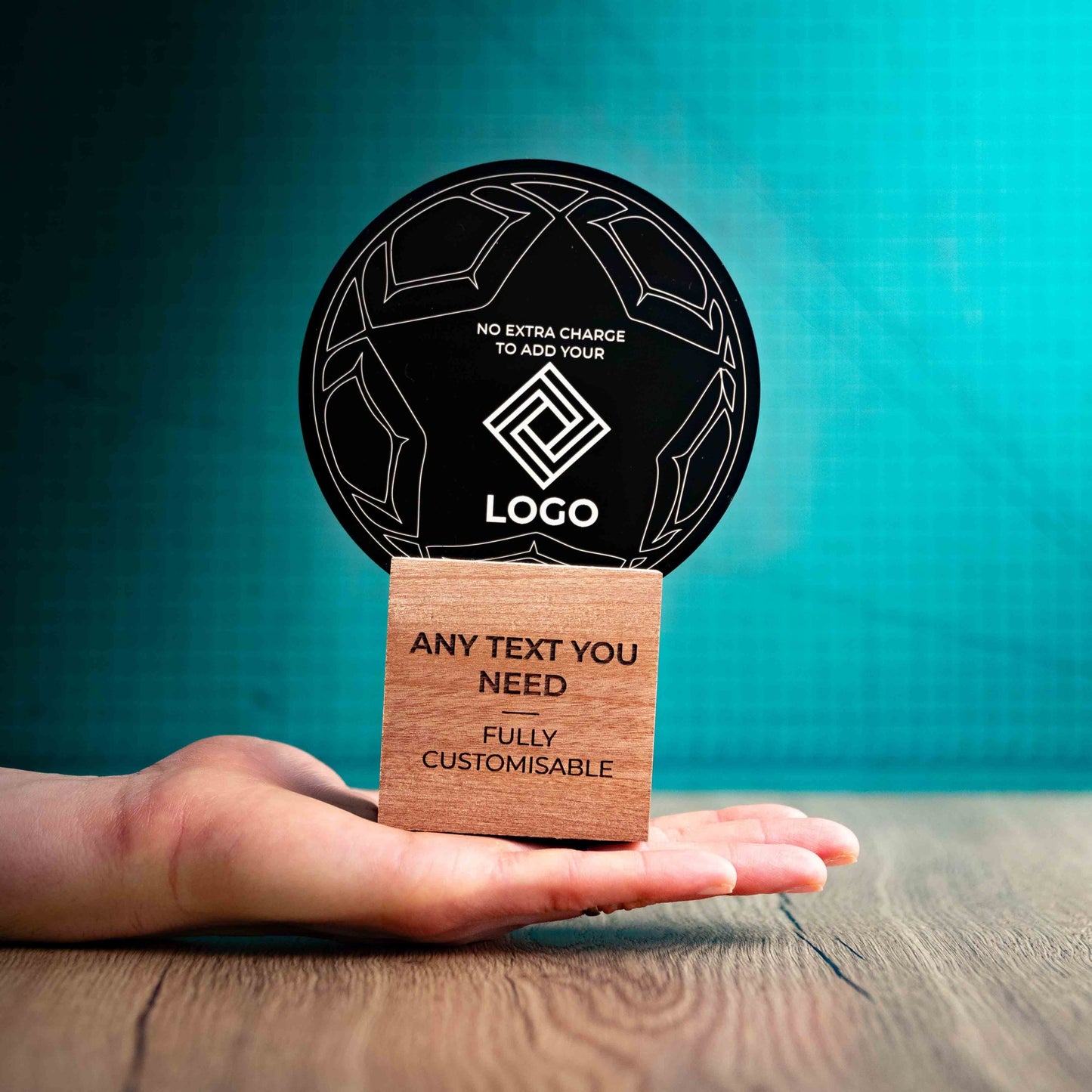 A hand holding a medium football trophy with custom text and logos, on an eco-friendly wooden base, with a black Perspex football mounted on top, featuring fully customisable areas for text and logos.