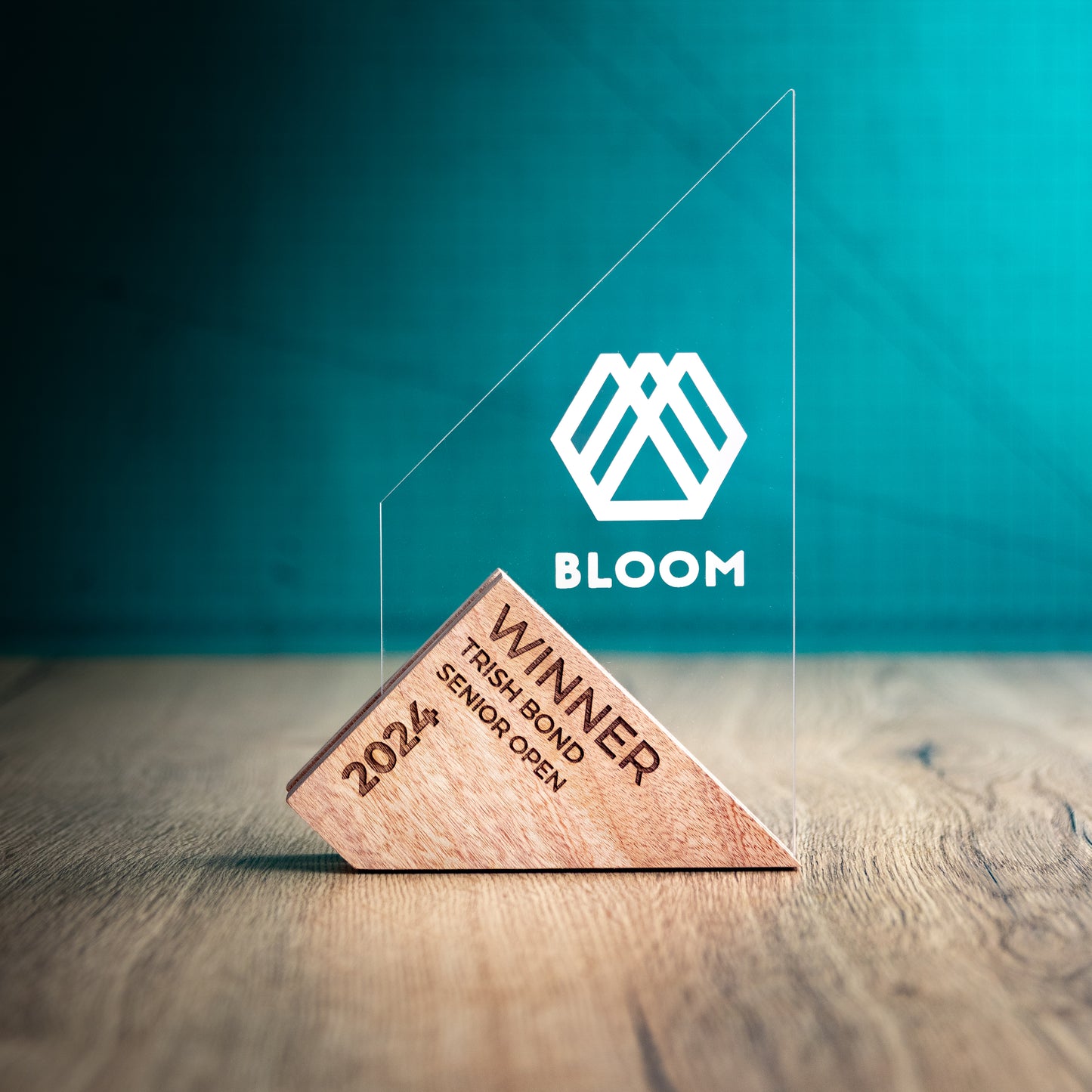A Large Genoa Award. An Eco-Friendly Wooden and Perspex Award that has a wooden base engraved with a logo and a recyclable clear Perspex triangular shape with a point on the left side of the trophy, which contains the winner and event information.