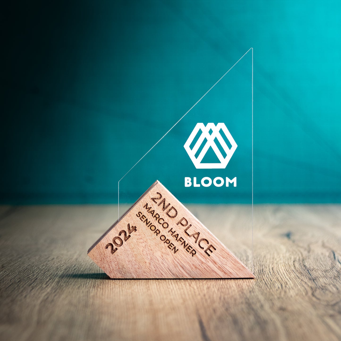 A Medium Genoa Award. An Eco-Friendly Wooden and Perspex Award that has a wooden base engraved with a logo and a recyclable clear Perspex triangular shape with a point on the left side of the trophy, which contains the winner and event information.