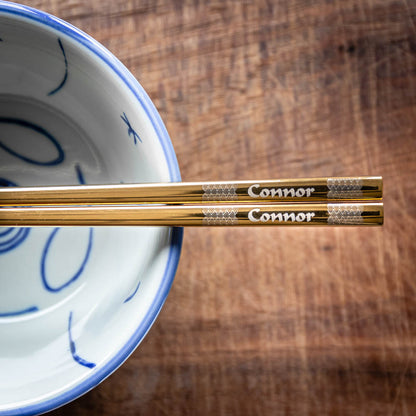 A pair of Chinese-style Metal Coloured Chopsticks - Gold. Each pair is personalised with either a name or a phrase.