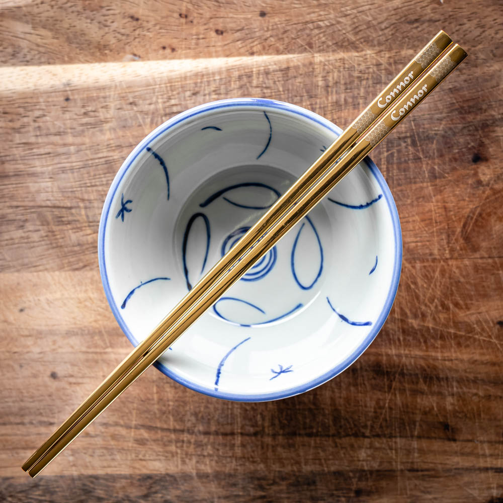 A pair of Chinese-style Metal Coloured Chopsticks - Gold. Each pair is personalised with either a name or a phrase.
