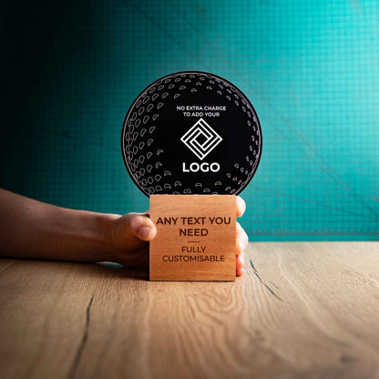 A hand holding a large golf award trophy with custom text and logos, on an eco-friendly wooden base, with a black Perspex golf ball mounted on top, with fully customisable areas featuring fully customisable areas for text and logos.