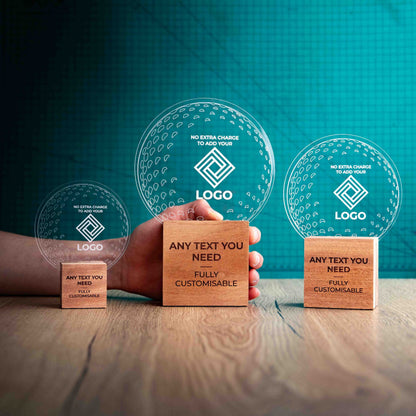 Three golf award trophies with custom text and logos, on eco-friendly wooden bases, with a clear Perspex golf ball mounted on top, with fully customisable areas featuring fully customisable areas for text and logos. A hand is present to show the size of the awards. 