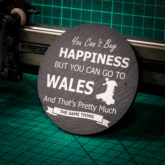 A laser engraved Welsh slate coaster with the words you can't buy happiness but you can go to Wales and that's pretty much the same thing