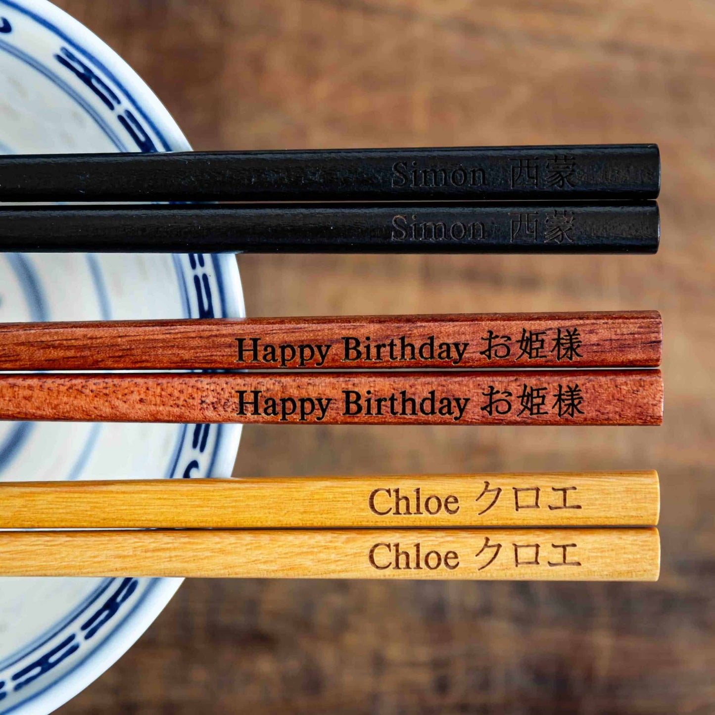 Three pairs of Japanese-style Chopsticks, Black wood, Rose wood and Light wood. Each pair is personalised with either a name or a phrase in English and is translated into either Chinese or Japanese.