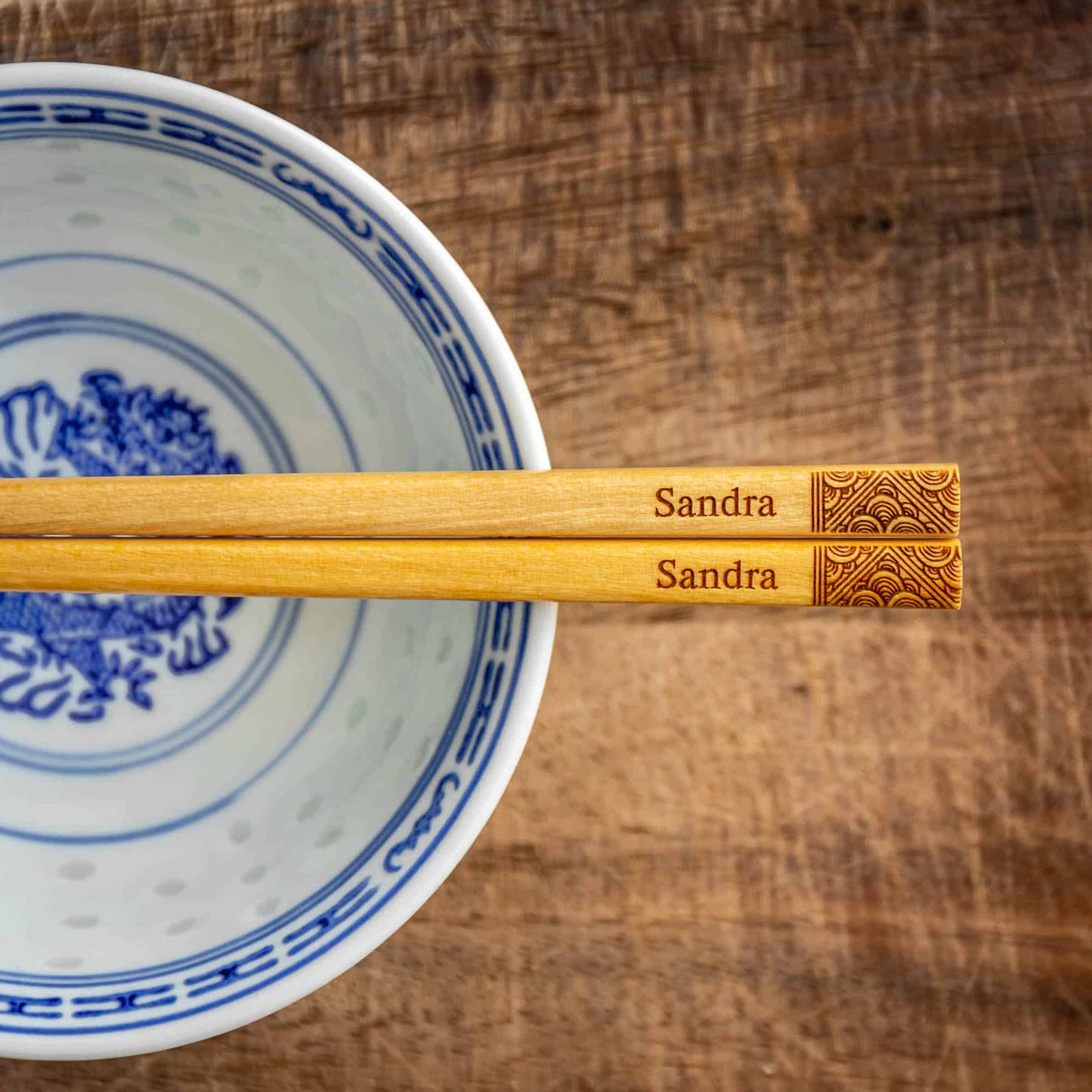 A pair of Japanese-style Chopsticks, Light wood. The pair is personalised with either a name or a phrase in English, translated into either Chinese or Japanese, and features a contemporary design at the end of the chopsticks.