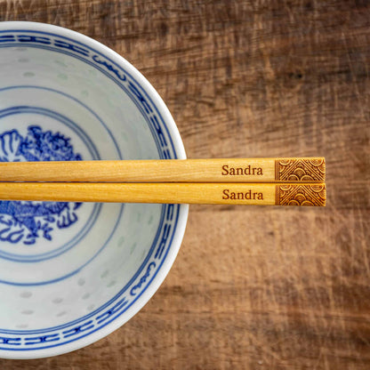 A pair of Japanese-style Chopsticks, Light wood. The pair is personalised with either a name or a phrase in English, translated into either Chinese or Japanese, and features a contemporary design at the end of the chopsticks.