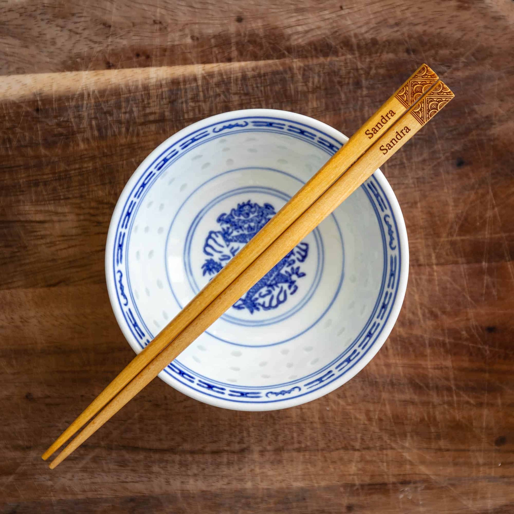A pair of Japanese-style Chopsticks, Light wood. The pair is personalised with either a name or a phrase in English, translated into either Chinese or Japanese, and features a contemporary design at the end of the chopsticks.