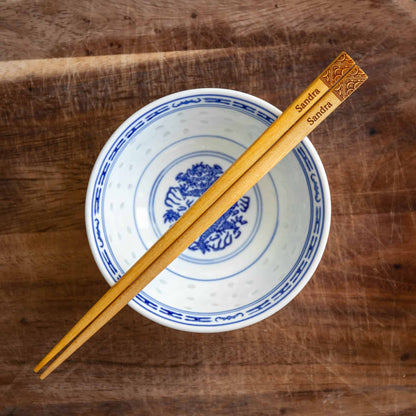 A pair of Japanese-style Chopsticks, Light wood. The pair is personalised with either a name or a phrase in English, translated into either Chinese or Japanese, and features a contemporary design at the end of the chopsticks.