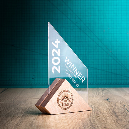 A Jib Award. An Eco-Friendly Wooden and Perspex Award that has a wooden base engraved with a logo and a recyclable clear Perspex triangular shape with a point on the right side of the trophy, which contains the winner and event information.