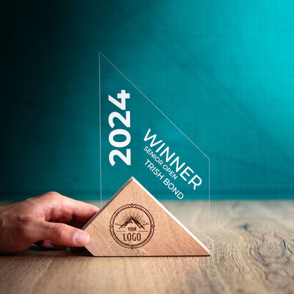 A Large Jib Award being held to give a size perspective. An Eco-Friendly Wooden and Perspex Award that has a wooden base engraved with a logo and a recyclable clear Perspex triangular shape with a point on the right side of the trophy, which contains the winner and event information.