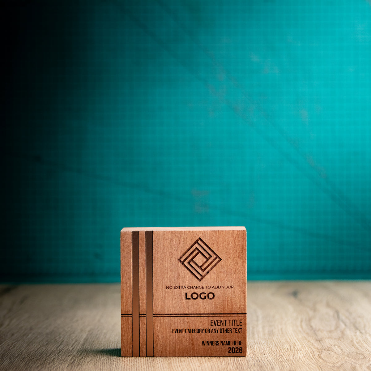 Front view of the small square Kingdom wooden trophy with two parallel bronze-toned metallic inlays running the full height of the left side, alongside engraved logo, event details, winner name and year.