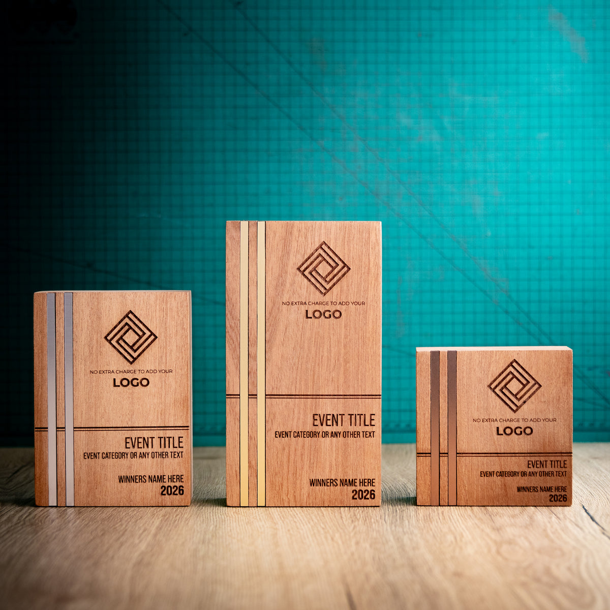 Three personalised Kingdom wooden trophies in small, medium and large sizes, each with two full-height metallic inlays set flush into the left side of the front face. The tall gold, medium silver and square bronze versions show engraved logos, event details and winner information.