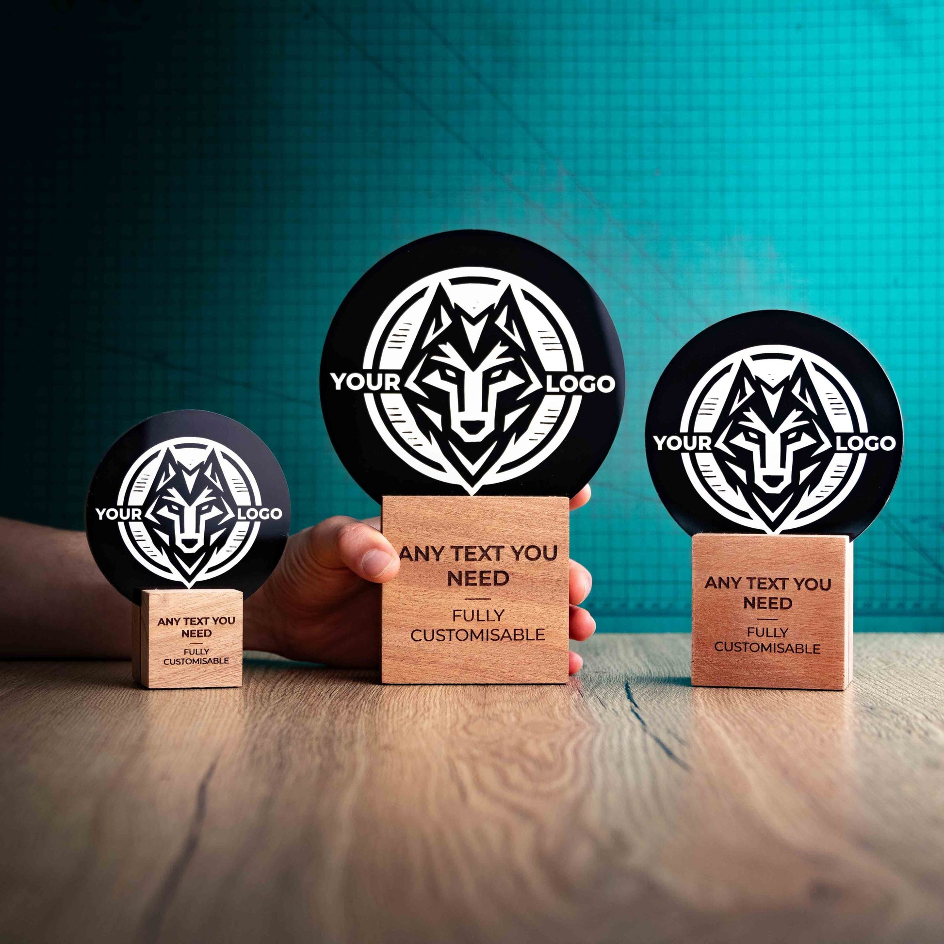 Three Legacy trophies with custom text and logos, on eco-friendly wooden bases, with a black Perspex circle mounted on top, featuring fully customisable areas for text and logos with a hand holding the large trophy to give a perspective of the size.