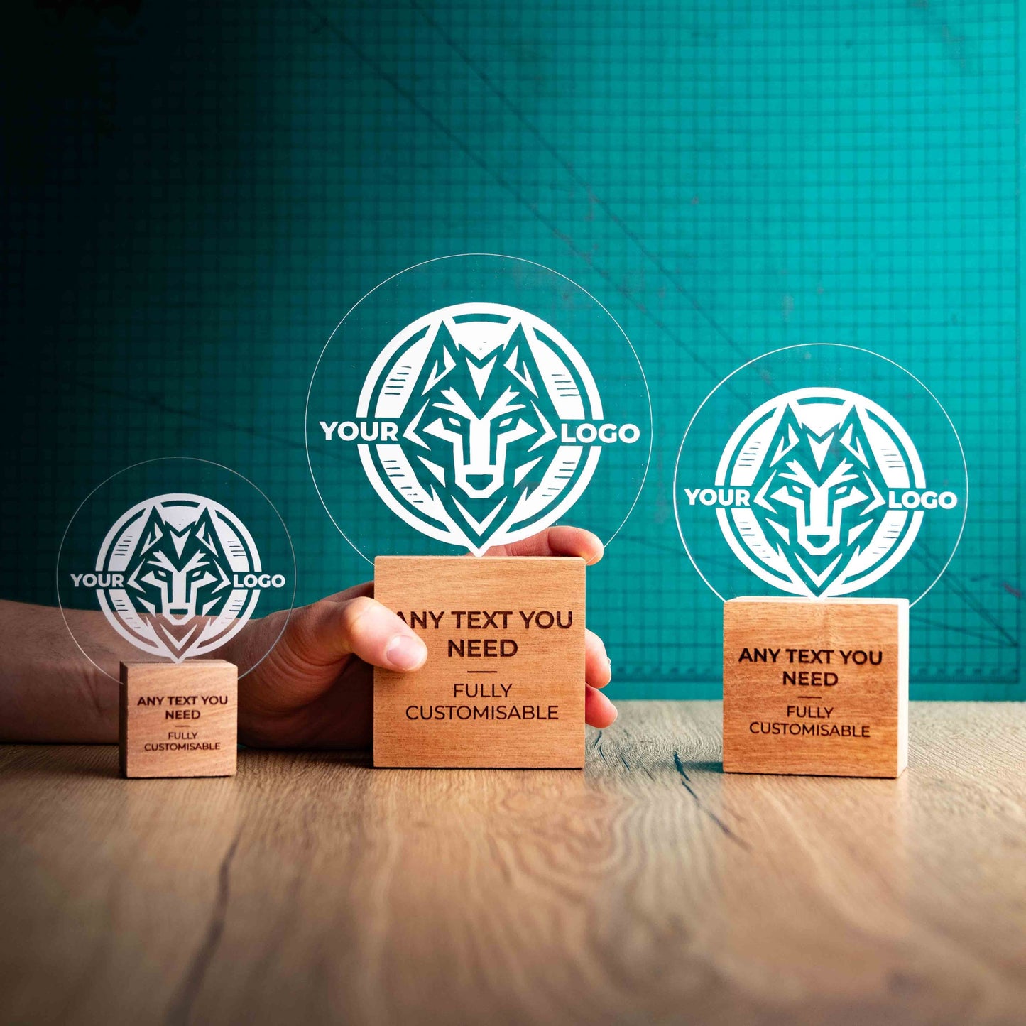 Three Legacy trophies with custom text and logos, on eco-friendly wooden bases, with a clear Perspex circle mounted on top, featuring fully customisable areas for text and logos, with a hand holding the large trophy to give a perspective of the size.