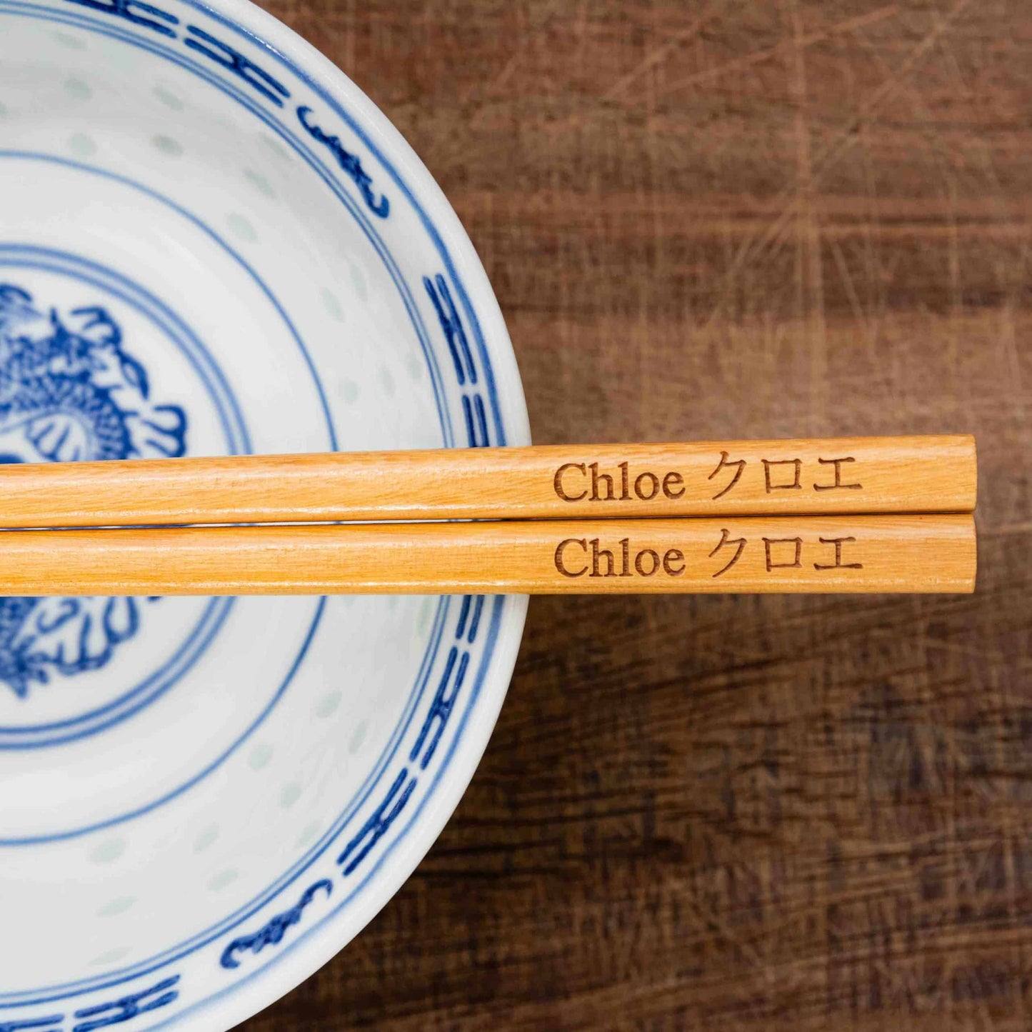 A pair of Japanese-style Chopsticks, colour light wood. The chopsticks are laser engraved and personalised with either a name or a phrase in English and are translated into either Chinese or Japanese.
