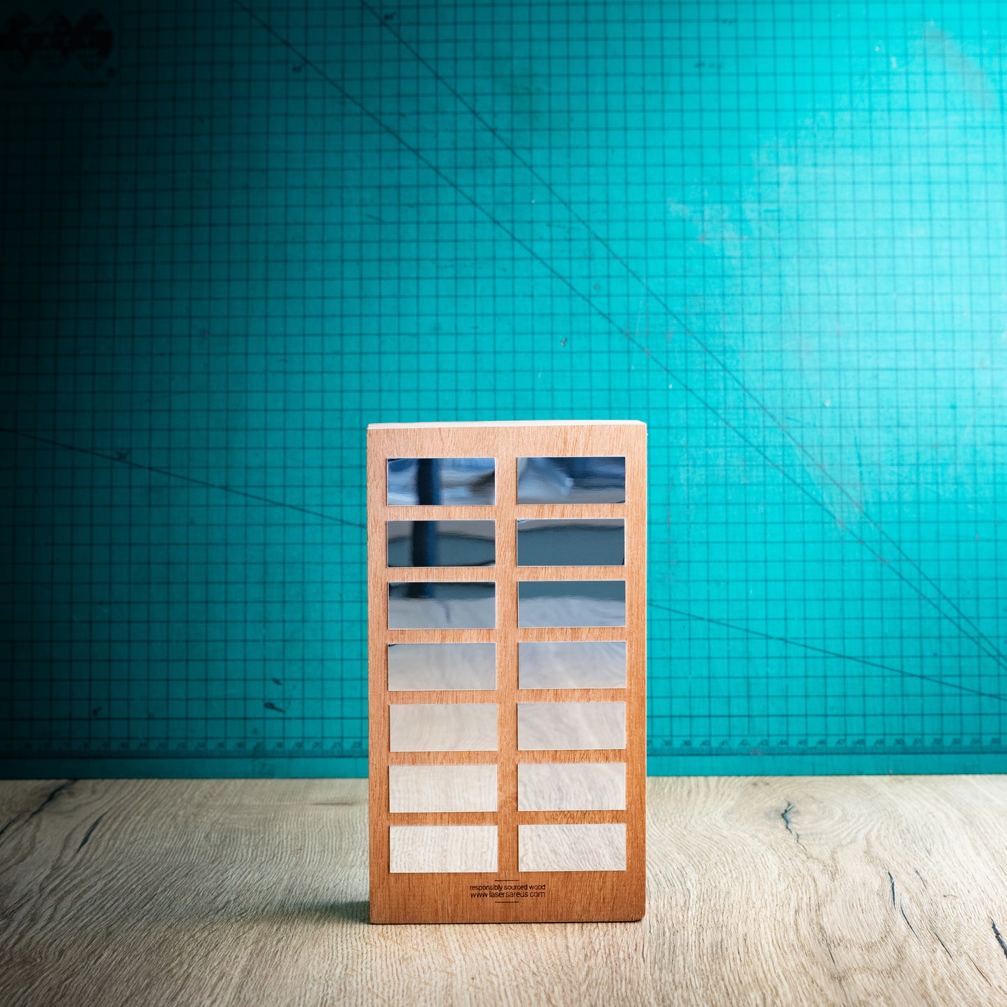 A rectangular wooden perpetual trophy with a grid of award plaques to engrave your winners names on, standing on a light wood surface against a teal background.