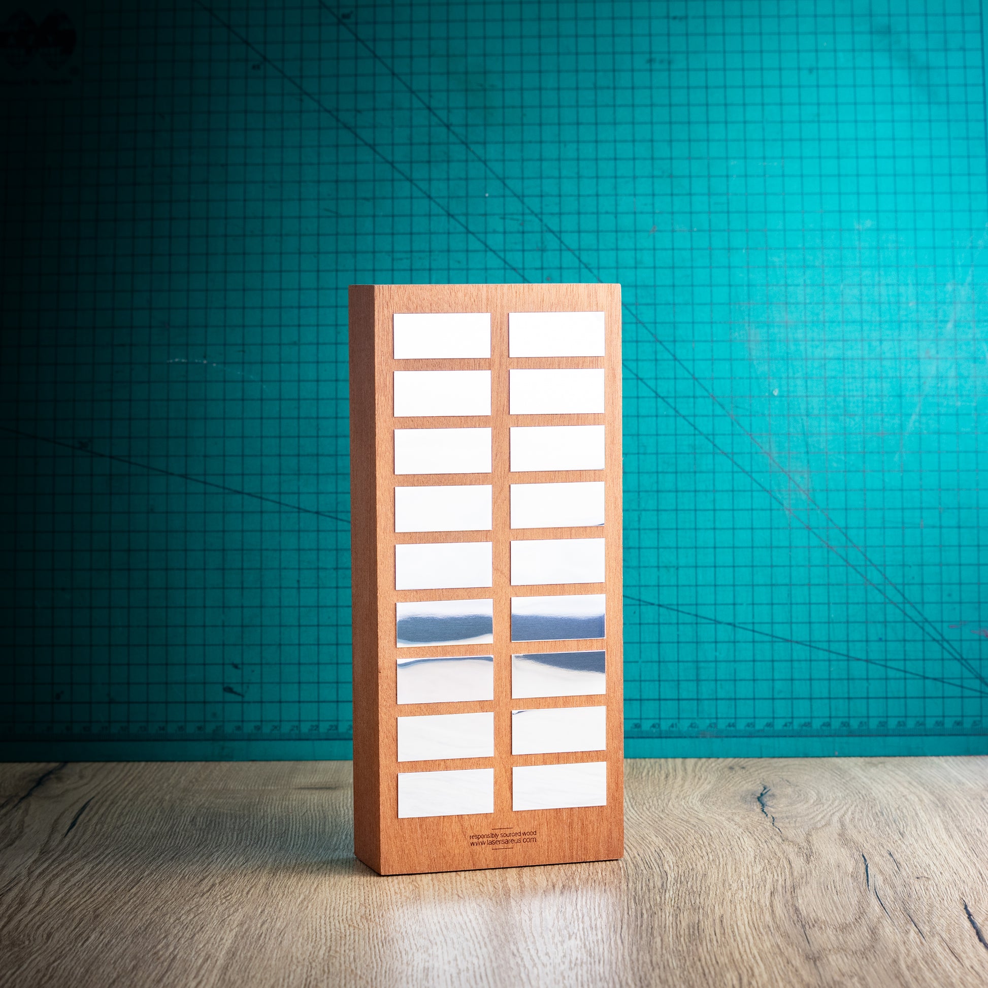 A rectangular wooden perpetual trophy with a grid of award plaques to engrave your winners names on, standing on a light wood surface against a teal background.