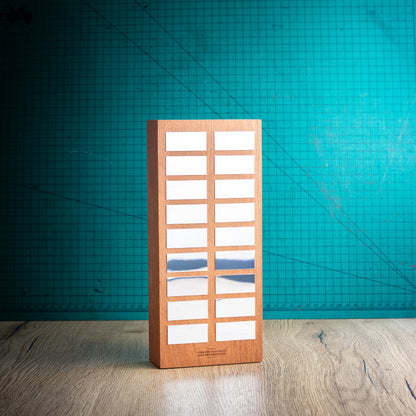 A rectangular wooden perpetual trophy with a grid of award plaques to engrave your winners names on, standing on a light wood surface against a teal background.