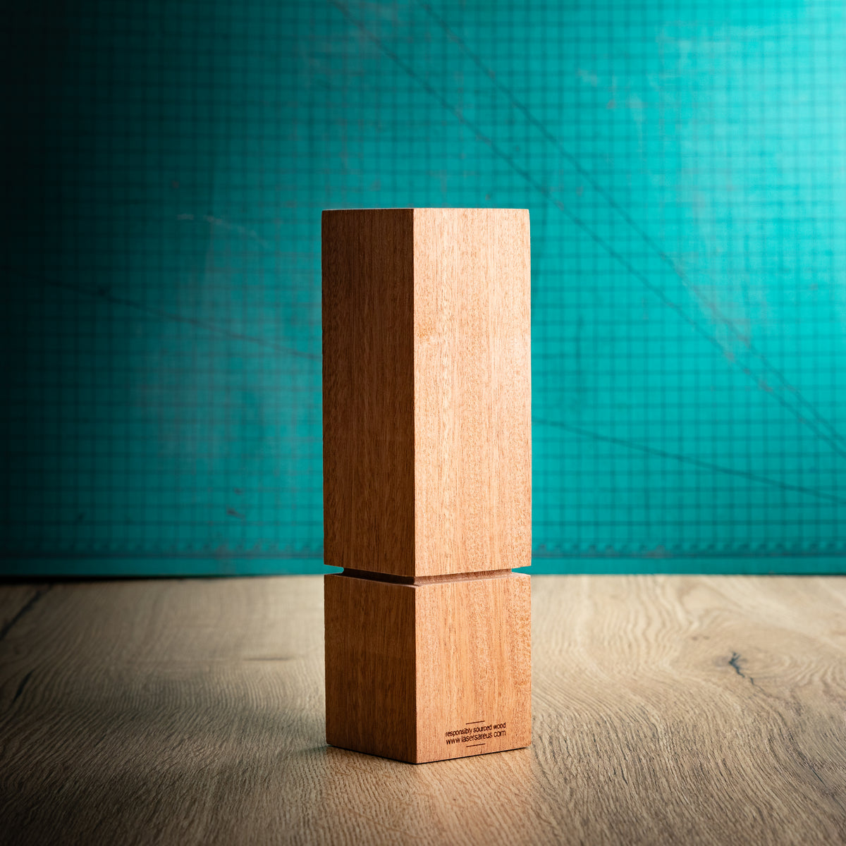A back view of square wooden block trophy with a distinctive recessed groove near the base, standing on a wooden surface against a textured teal background. The block is engraved with a geometric logo, placeholder text, and place rank: 1st, 2nd, and 3rd.