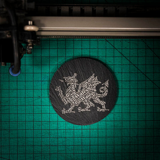 A laser engraved Welsh slate coaster with a dragon made up of the words Wales and Cymru