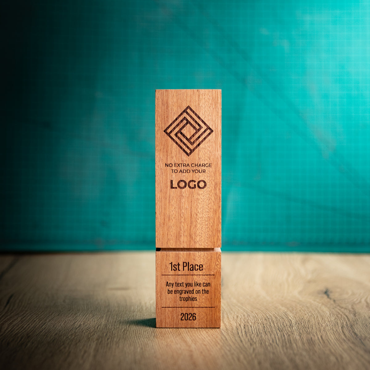 A square wooden block trophy with a distinctive recessed groove near the base, standing on a wooden surface against a textured teal background. The block is engraved with a geometric logo, placeholder text, and place rank: 1st, 2nd, and 3rd.