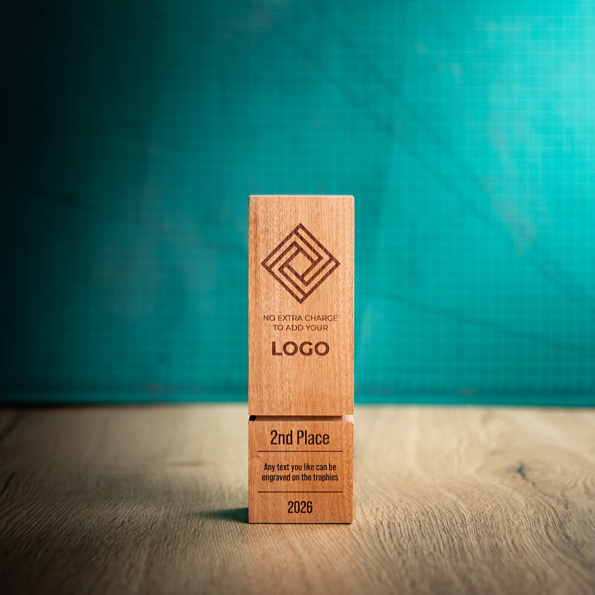 A square wooden block trophy with a distinctive recessed groove near the base, standing on a wooden surface against a textured teal background. The block is engraved with a geometric logo, placeholder text, and place rank: 1st, 2nd, and 3rd.