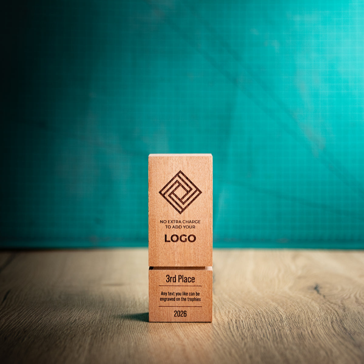 A square wooden block trophy with a distinctive recessed groove near the base, standing on a wooden surface against a textured teal background. The block is engraved with a geometric logo, placeholder text, and place rank: 1st, 2nd, and 3rd.