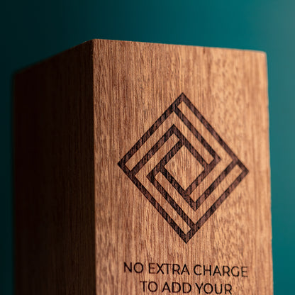 A close-up of a wooden block or plaque with a laser-engraved geometric diamond pattern and the text 'NO EXTRA CHARGE TO ADD YOUR'.