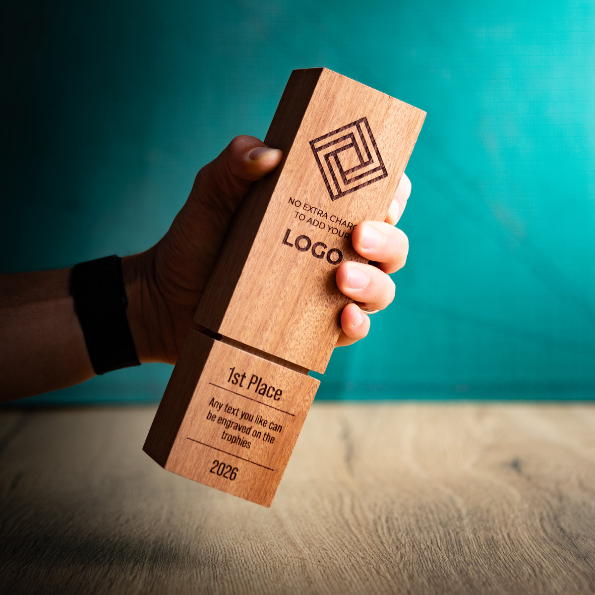 A square wooden block trophy with a distinctive recessed groove near the base, held in a hand to give a size perspective. The block is engraved with a geometric logo, placeholder text, and place rank: 1st, 2nd, and 3rd.