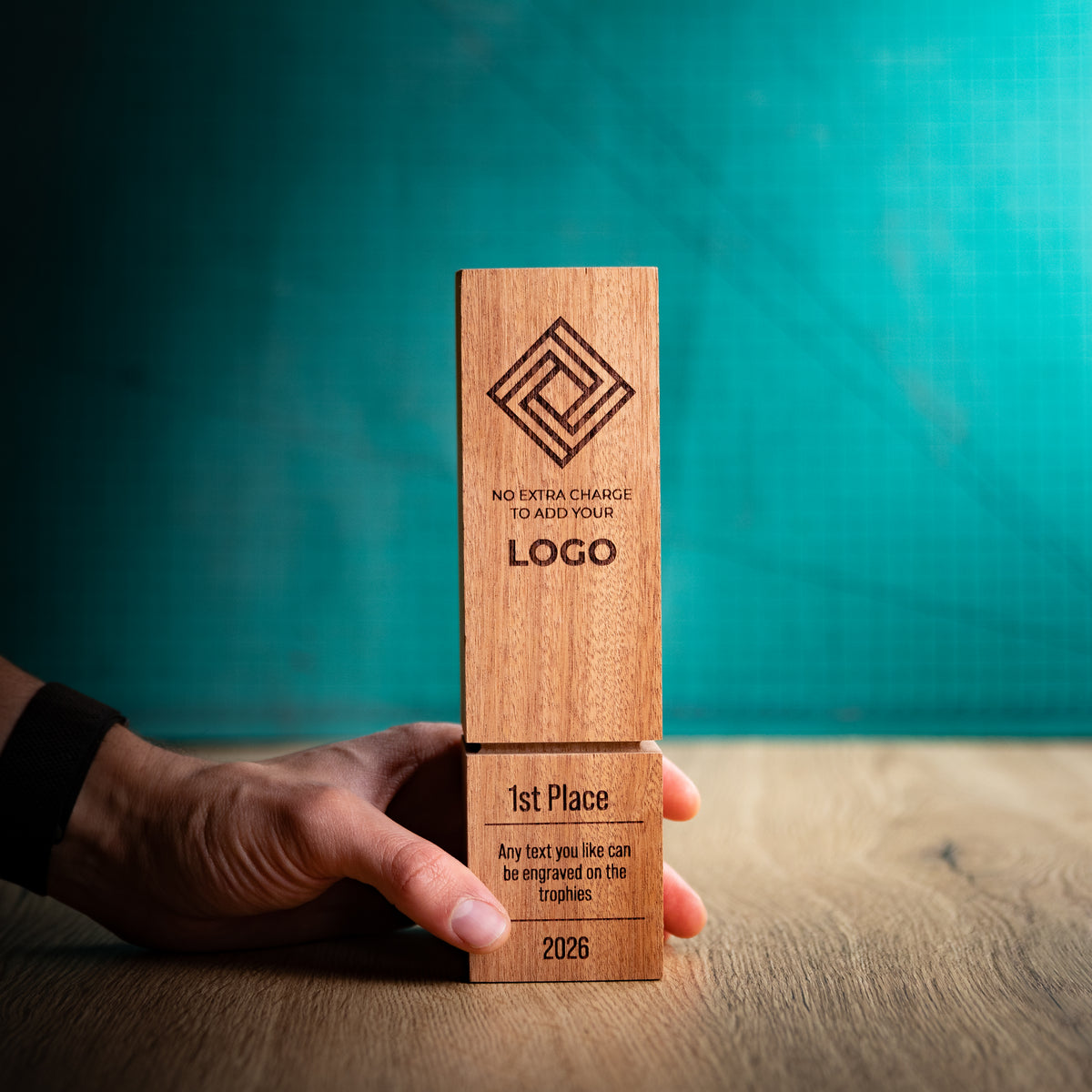 A square wooden block trophy with a distinctive recessed groove near the base, held in a hand to give a size perspective. The block is engraved with a geometric logo, placeholder text, and place rank: 1st, 2nd, and 3rd.