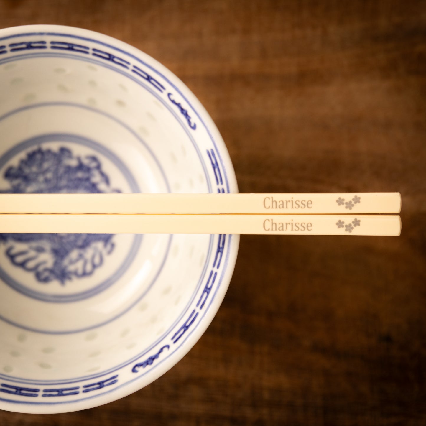Cream coloured plastic melamine personalised chopsticks engraved with a name and three flowers.