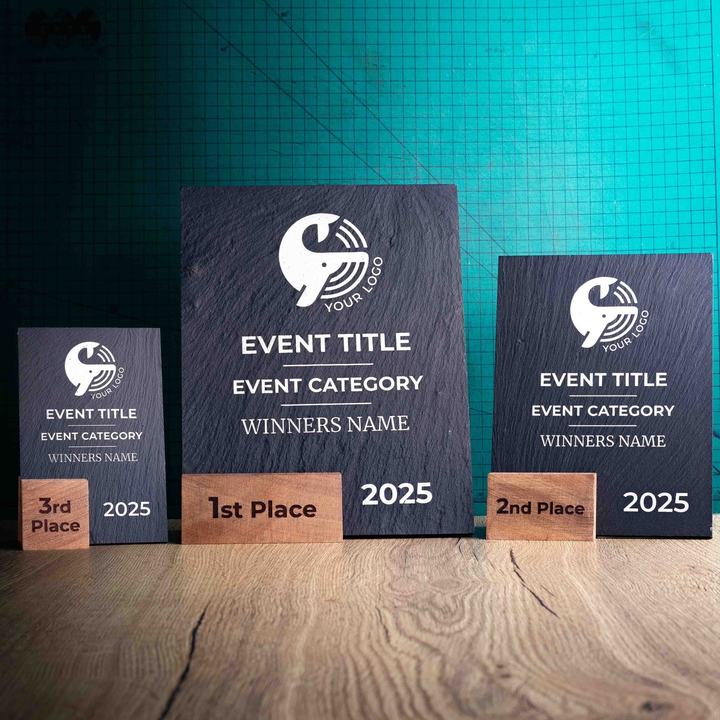 Three laser-engraved, eco-friendly, wooden and slate trophies called Solet. The Solet Award has a base made of two wooden pieces on either side of a square piece of Welsh Slate. The trophy is personalised with Event information and a logo. 