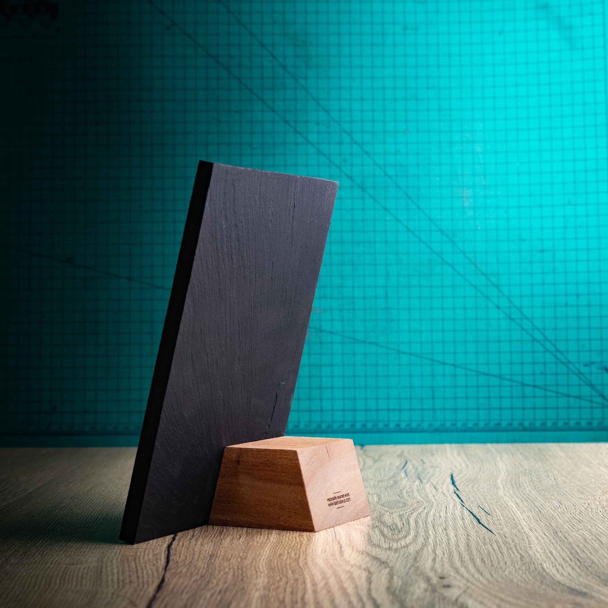 A side angle of a Medium Solet Award, an eco-friendly, wooden and slate trophy. The Solet Award has a base made of two wooden pieces on either side of a square piece of Welsh Slate. The trophy is personalised with Event information and a logo. 
