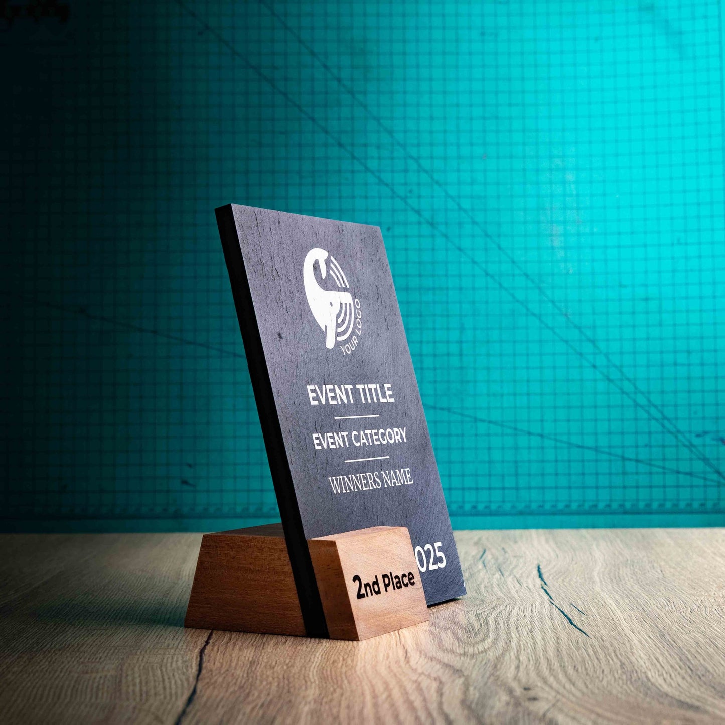 A side angle of a Medium Solet Award, an eco-friendly, wooden and slate trophy. The Solet Award has a base made of two wooden pieces on either side of a square piece of Welsh Slate. The trophy is personalised with Event information and a logo. 