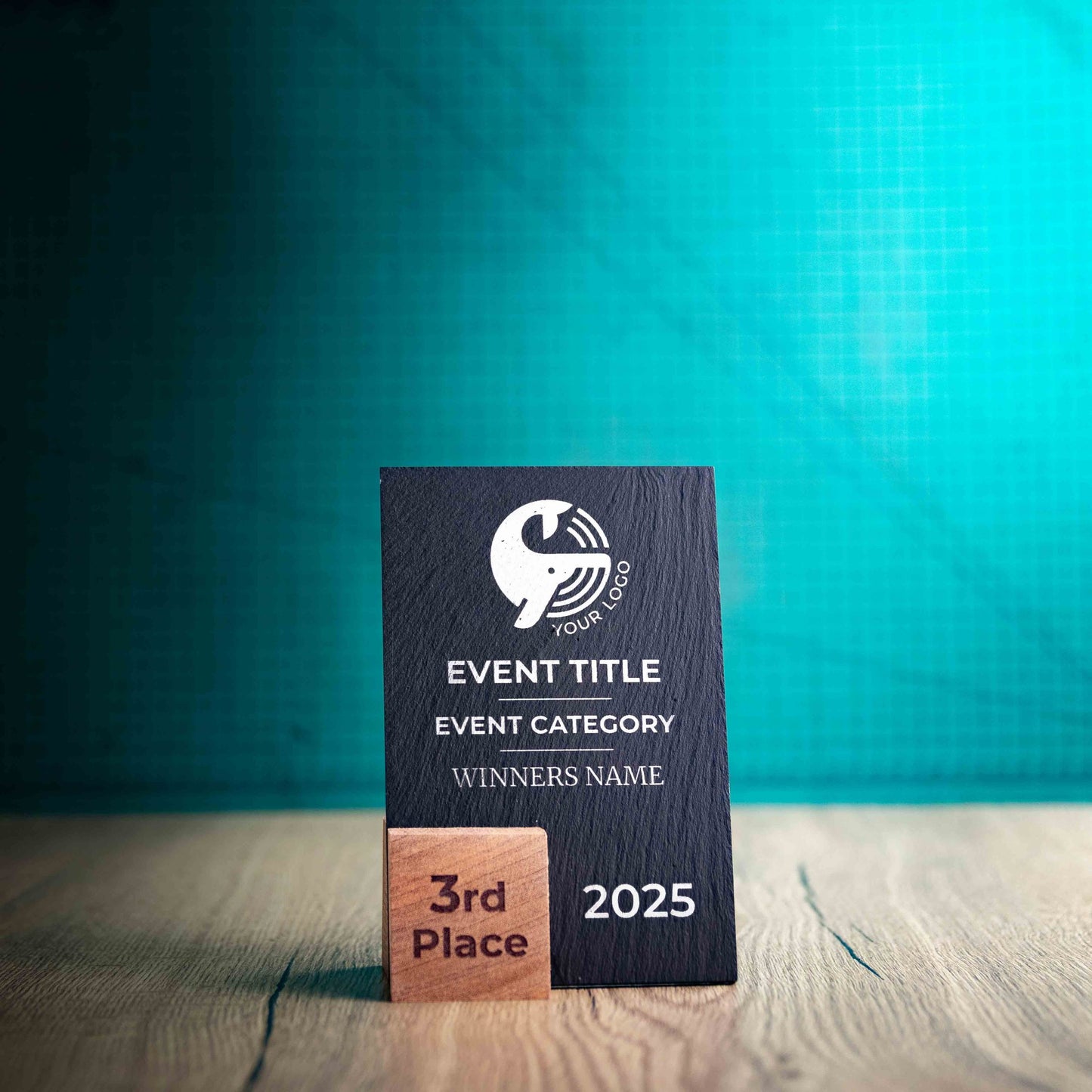 A small Solet Award, an eco-friendly, wooden and slate trophy. The Solet Award has a base made of two wooden pieces on either side of a square piece of Welsh Slate. The trophy is personalised with Event information and a logo. 
