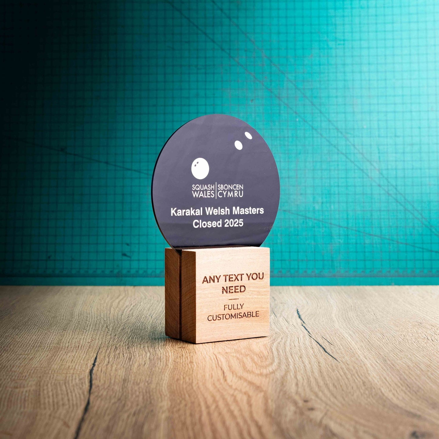 The side view of a medium Squash trophy with custom text and logos, on an eco-friendly wooden base, with a black Perspex Squash ball mounted on top, featuring fully customisable areas for text and logos.