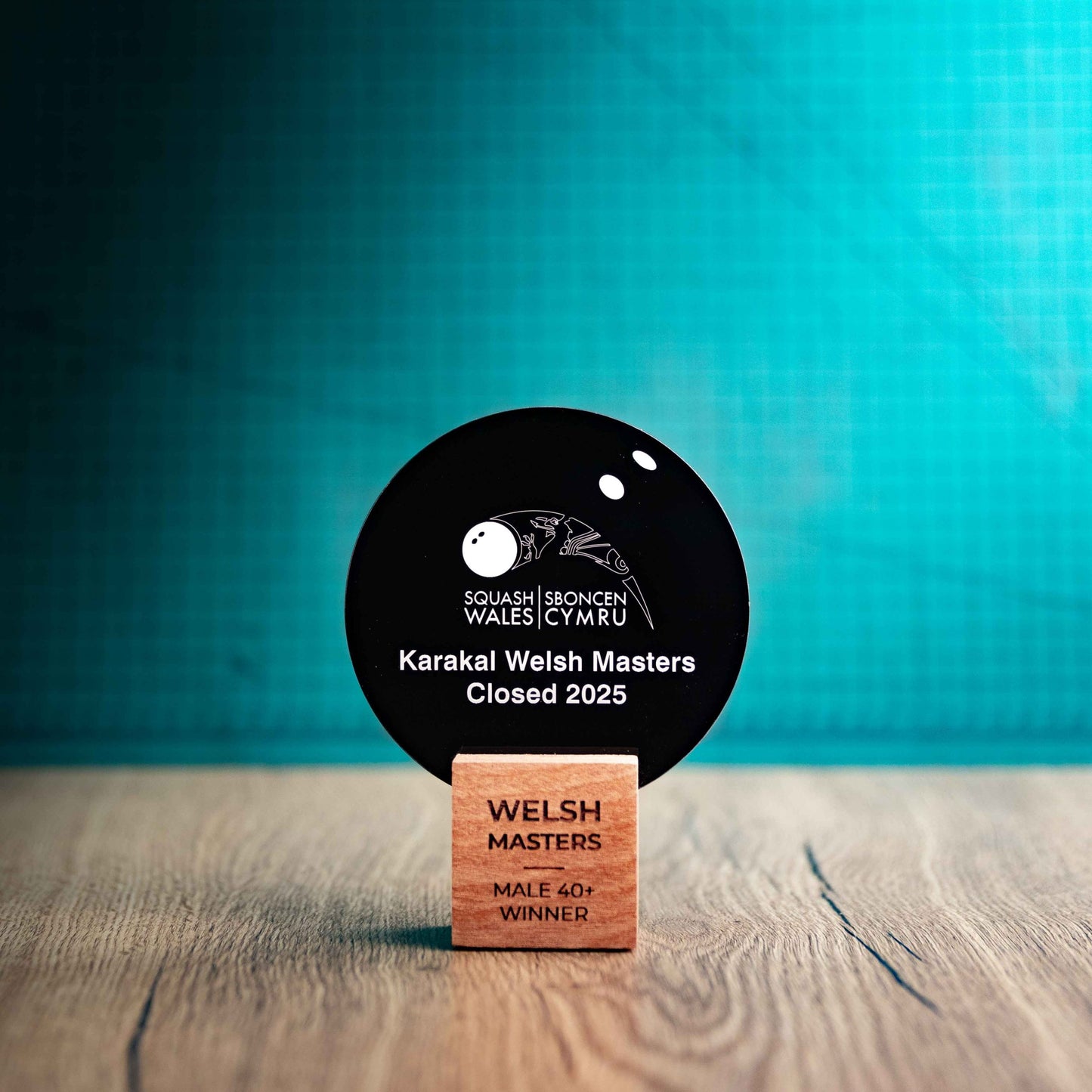 A medium Squash trophy with custom text and logos, on an eco-friendly wooden base, with a black Perspex Squash ball mounted on top, featuring fully customisable areas for text and logos.