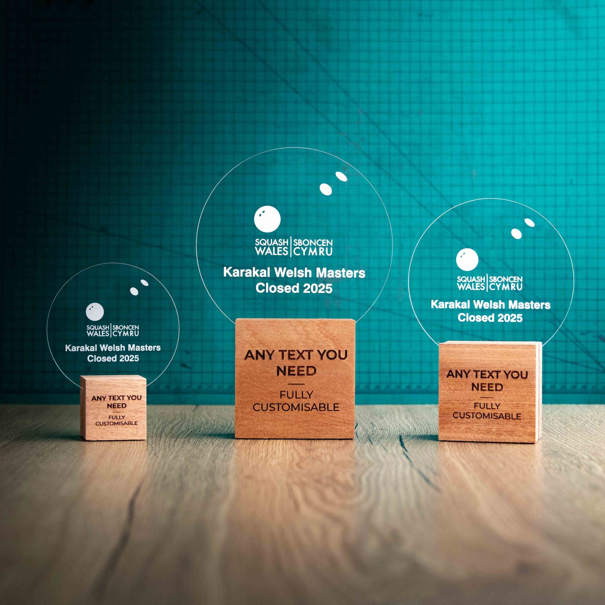 Three squash trophies with custom text and logos, on eco-friendly wooden bases, with a clear Perspex squash ball mounted on top, featuring fully customisable areas for text and logos.
