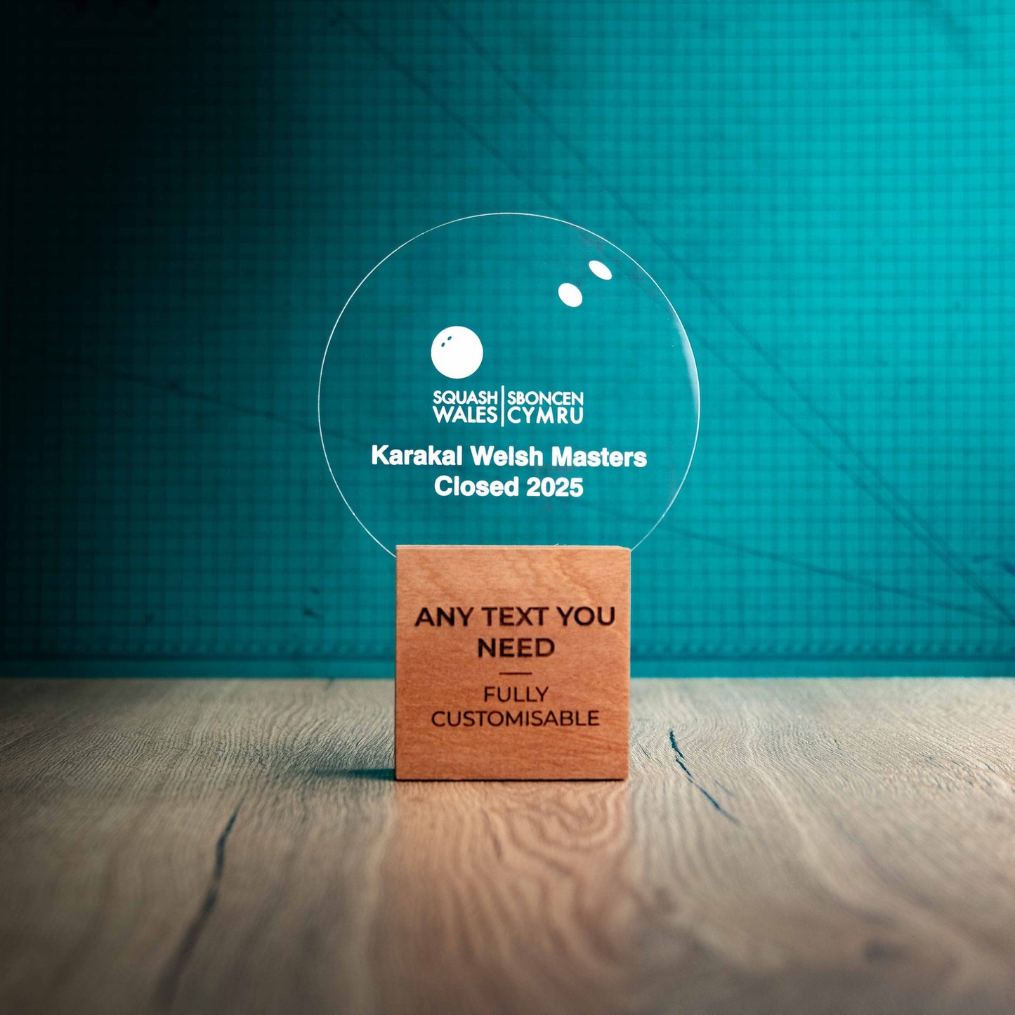 A large Squash trophy with custom text and logos, on an eco-friendly wooden base, with a clear Perspex Squash ball mounted on top, featuring fully customisable areas for text and logos.
