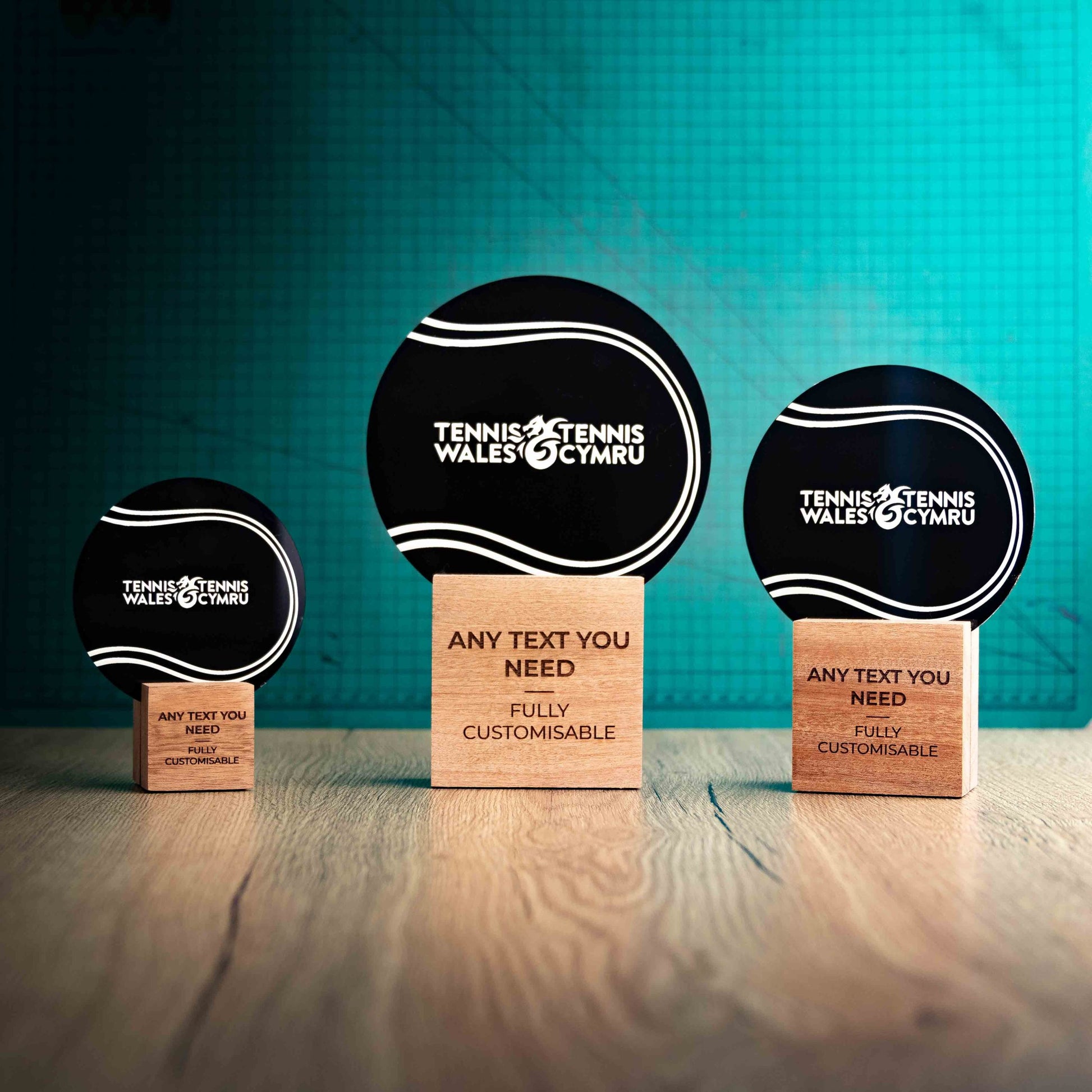 Three Tennis trophies with custom text and logos, on eco-friendly wooden bases, with a black Perspex Tennis Ball mounted on top, featuring fully customisable areas for text and logos.