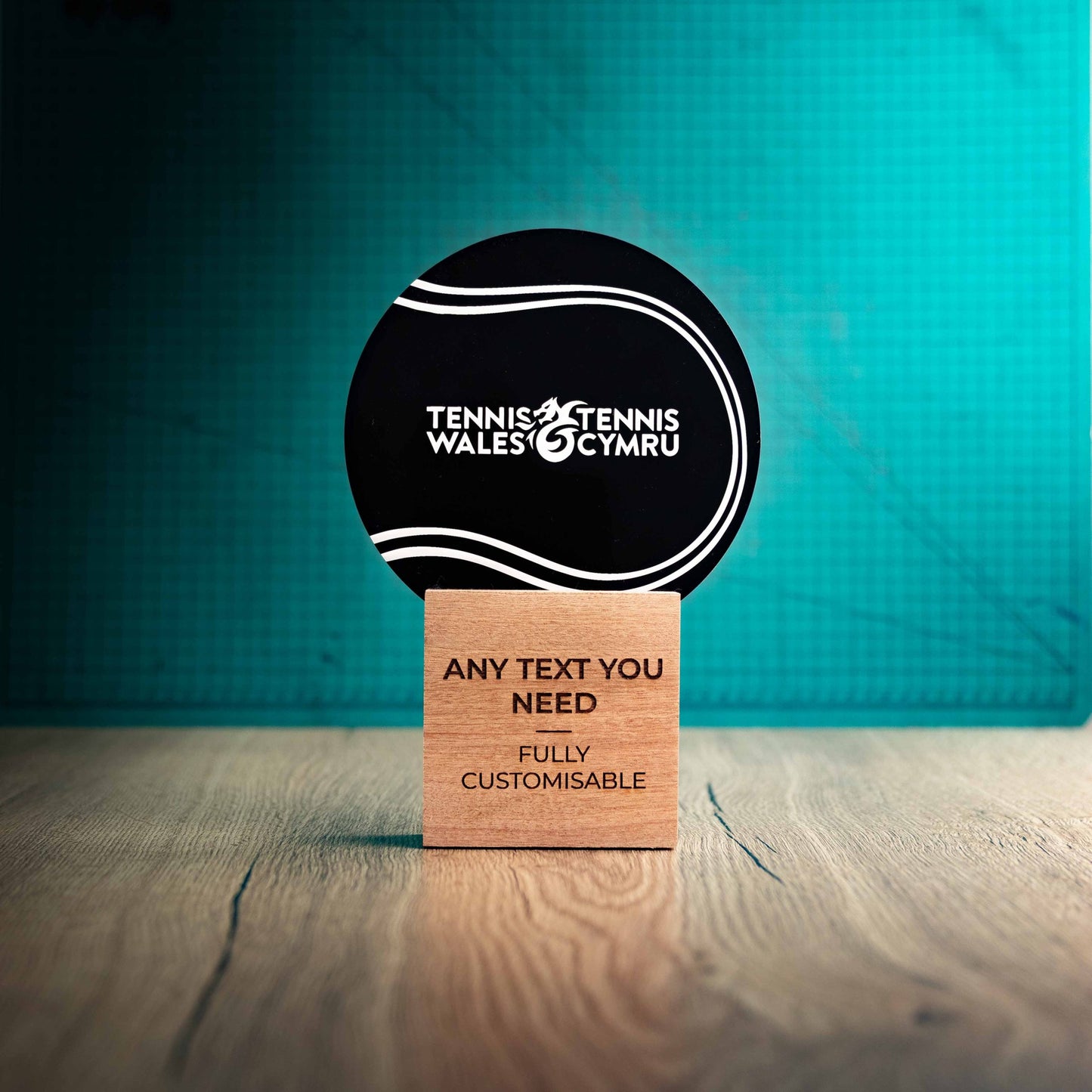 A large Tennis trophy with custom text and logos, on an eco-friendly wooden base, with a black Perspex Tennis ballmounted on top, featuring fully customisable areas for text and logos.