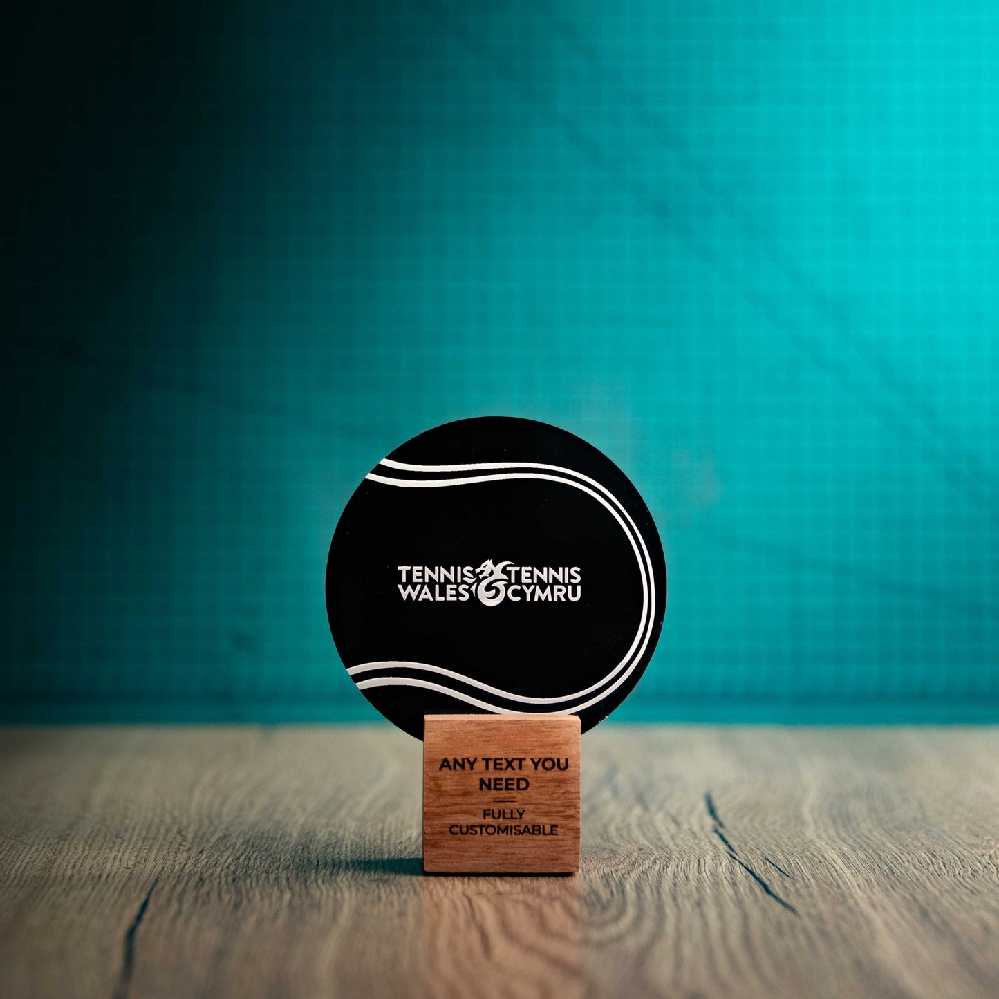 A small Tennis trophy with custom text and logos, on an eco-friendly wooden base, with a black Perspex Tennis ballmounted on top, featuring fully customisable areas for text and logos.