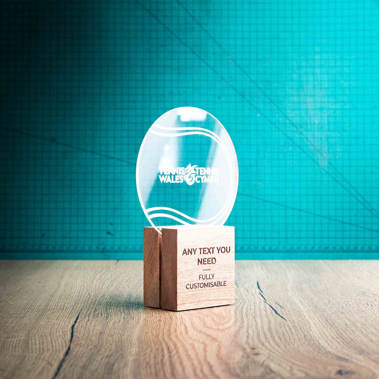 A side view of a medium Tennis trophy with custom text and logos, on an eco-friendly wooden base, with a clear Perspex Tennis ball mounted on top, featuring fully customisable areas for text and logos.